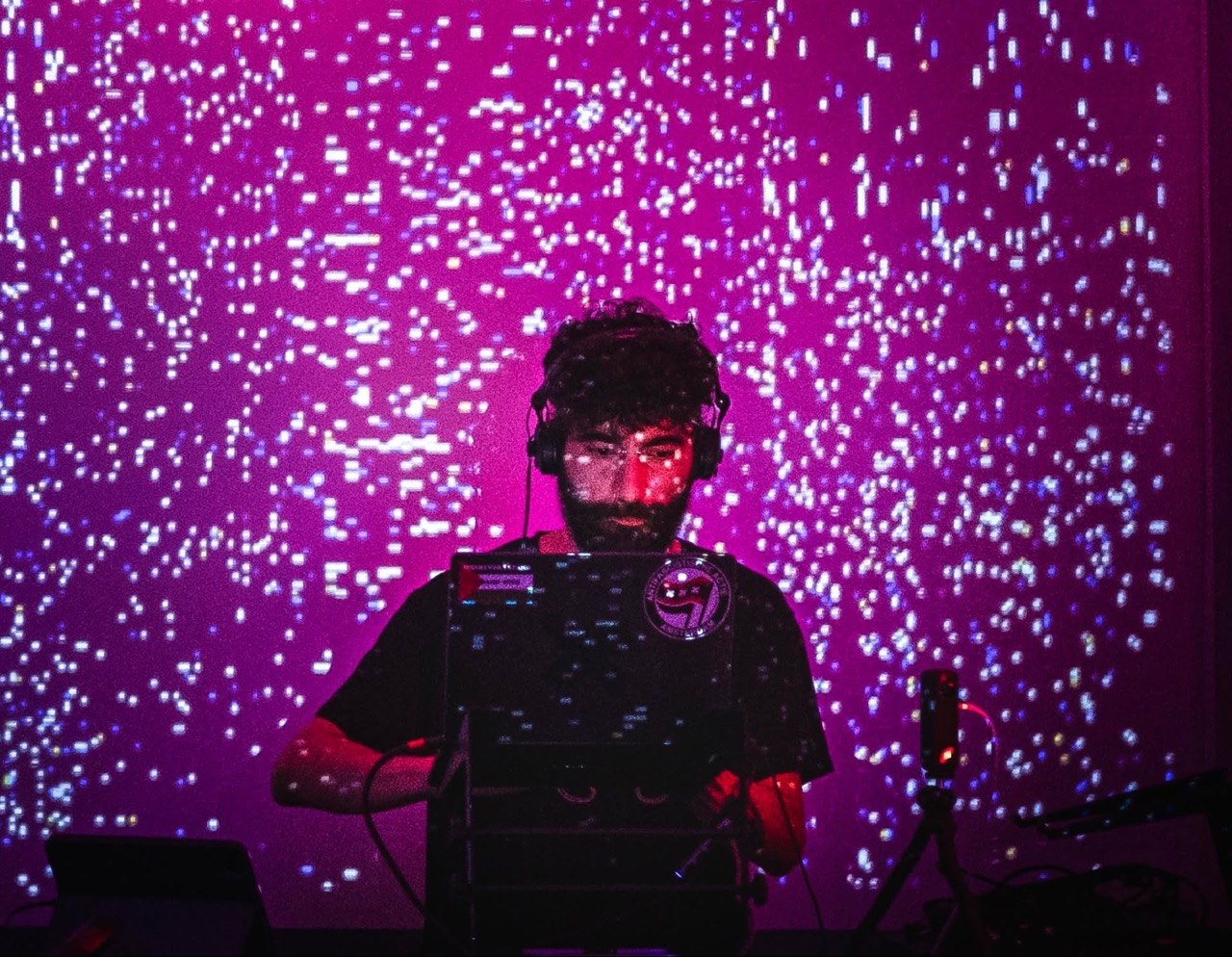SPITS performing behind a laptop in front of a magenta projection wall